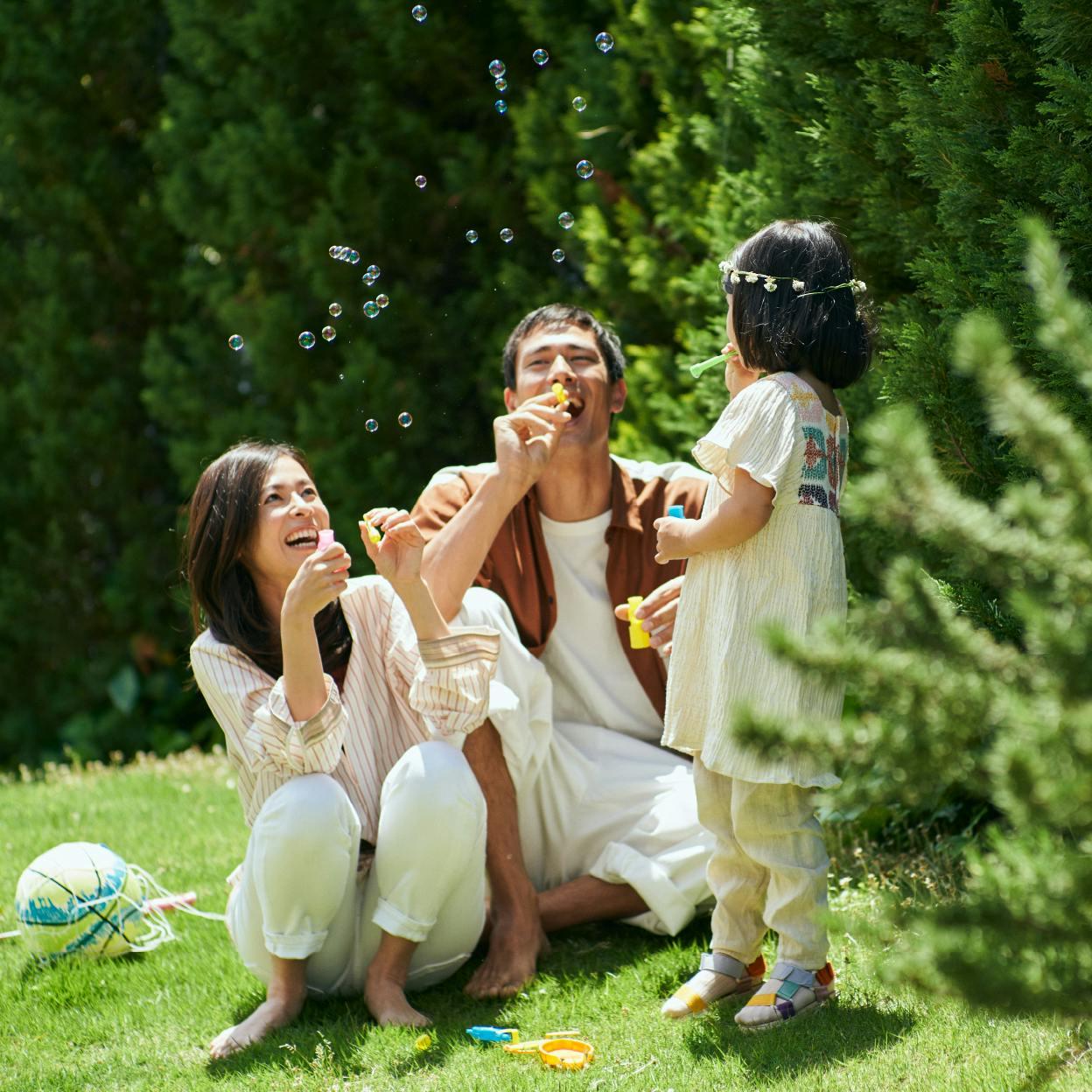 緑の綺麗な公園でシャボン玉を吹く母親と父親と娘